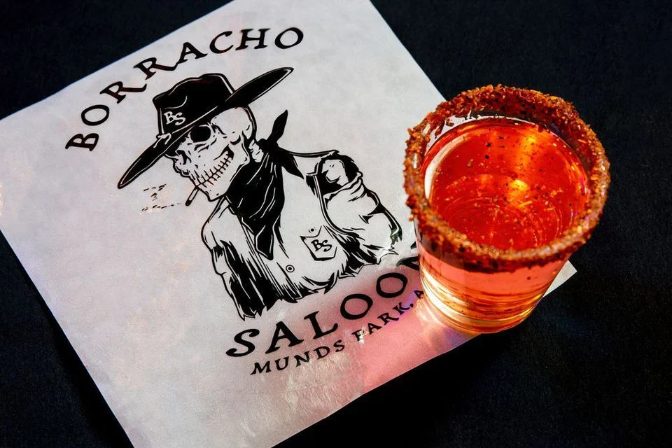 Aerial view of a chamoy lined, orange-red shot sitting on the bottom right corner of a Borracho Saloon napking